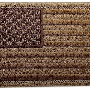 Pode incluir: Um remendo de bandeira americana bordado em marrom com uma borda bege. As estrelas são marrons e as listras são bege.