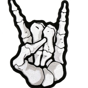 Może przedstawiać: Biała szkieletowa dłoń wykonująca gest rock and roll. Dłoń jest obwiedziona czernią.