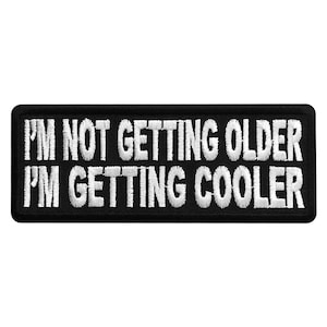 May include: Black embroidered patch with white text that reads "I'm not getting older I'm getting cooler".