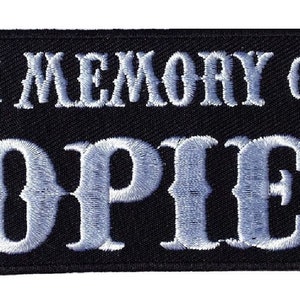 Könnte beinhalten: Schwarzer gestickter Aufnäher mit weißem Text, der "In Memory of 'Opie'" lautet.