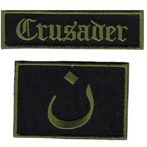 Könnte beinhalten: Zwei gestickte Aufnäher. Der erste Aufnäher ist grün mit schwarzem Text, der "Crusader" lautet. Der zweite Aufnäher ist schwarz mit einem grünen arabischen Buchstaben.