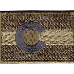 May include: A brown and tan embroidered patch with a grey circle containing a white "C" in the centre. The patch is a representation of the Colorado state flag.