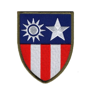 May include: Embroidered patch with a shield design. The top half is navy blue with a white star and a white sunburst. The bottom half features red and white vertical stripes. The patch has a green border.