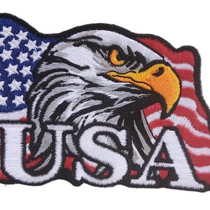 May include: Embroidered patch featuring a detailed bald eagle head with an orange beak and yellow eye, set against a waving American flag. The word "USA" is prominently displayed in white letters.