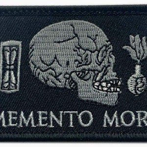 Może przedstawiać: Czarna naszywka haftowana z szarą czaszką, klepsydrą i kwiatem z sercem. Tekst "MEMENTO MORI" jest wyszyty pod obrazkiem.