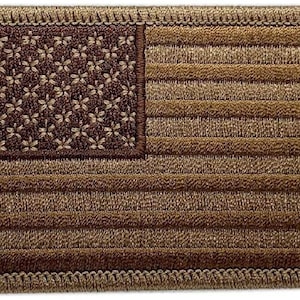 Pode incluir: Um remendo de bandeira americana bordado em marrom com uma borda bege. As estrelas são marrons e as listras são bege.