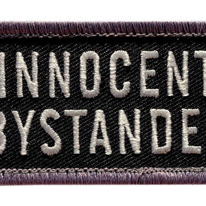 May include: Black patch with white embroidered text that reads "Innocent Bystander".
