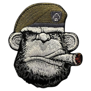 May include: Embroidered patch of a monkey wearing a green beret with a black and white insignia, smoking a cigar. The monkey has a serious expression and a thick black beard.