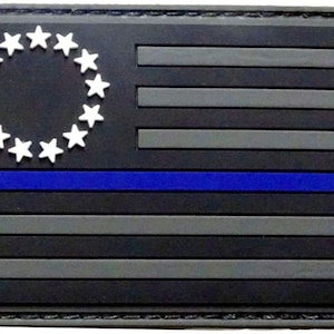 May include: Black and gray American flag patch with a blue line across the middle and 13 white stars in a circle in the top left corner.
