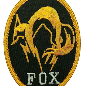 Pode incluir: Um remendo bordado preto e dourado com um design de raposa estilizado e a palavra "FOX" em letras brancas.