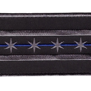 Könnte beinhalten: Ein gestickter schwarzer und grauer Aufnäher mit einer blauen Linie und fünf weißen Sternen. Der Aufnäher ist eine Darstellung der Flagge von Chicago.