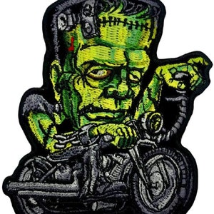 May include: Green Frankenstein monster riding a black motorcycle with a green and black design. The monster has stitches on its neck and a bolt in its head.