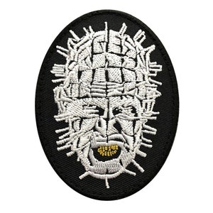May include: White embroidered patch of a face with a grid pattern and gold teeth on a black background.