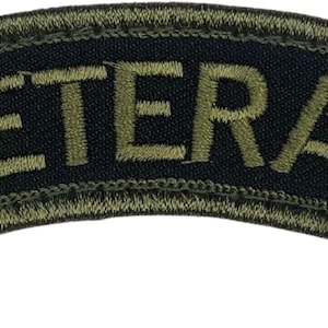 May include: A curved, embroidered patch with the word "VETERAN" in olive green thread. The text is centered on a navy blue background, with an olive green border. The patch has a military or service theme.