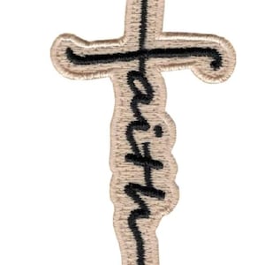 以下が含まれることがあります： 十字架の形をしたベージュ色の刺繍ワッペン。黒い筆記体で「faith」という文字が刺繍されており、文字の「t」が十字架の縦棒を形成しています。ワッペンの縁はベージュ色のステッチで仕上げられています。