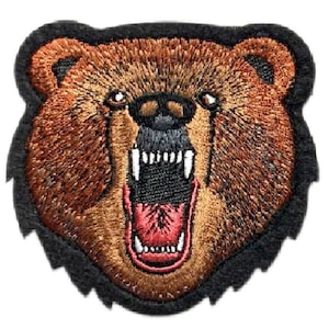 Peut inclure: Une tête d'ours brun sur un fond noir. L'ours a une grande gueule ouverte avec des dents acérées et une langue rouge. La fourrure de l'ours est détaillée avec une broderie brune et orange.