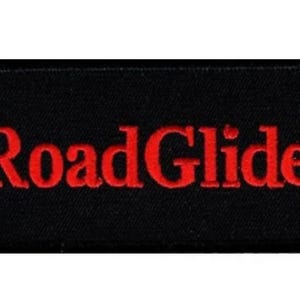 Peut inclure: Écusson rectangulaire noir aux coins arrondis. Le mot "RoadGlide" est brodé en rouge, en gras, en majuscules au centre. L'écusson a un aspect texturé et le fond est noir.