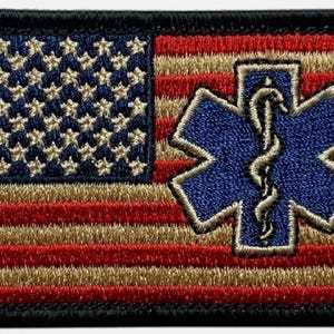 May include: Embroidered patch depicting the American flag with red and gold stripes, blue stars, and a blue Star of Life symbol. The patch has a black border, possibly for medical or emergency services.