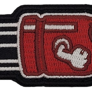 May include: Red and white embroidered iron-on patch of a video game character shaped like a bullet with a face and a white arm.