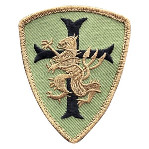 May include: Embroidered patch with a shield shape. The patch features a black cross with a tan lion-like creature in the center. The background is light green, and the border is tan.