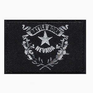 May include: A black embroidered patch featuring the state seal of Nevada. The seal is silver and depicts a star with the words "State of Nevada" around it.