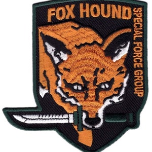 May include: A black and green embroidered patch featuring a fox head and a knife. The text "FOX HOUND SPECIAL FORCE GROUP" is on the patch.
