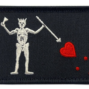 May include: Black embroidered patch featuring a white skeleton holding a spear, a red heart pierced by the spear, and three red dots. The skeleton is wearing a crown.