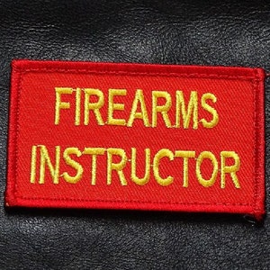 Könnte beinhalten: Roter Patch mit weißen Nähten und den Worten "FIREARMS INSTRUCTOR" in Gelb gestickt.