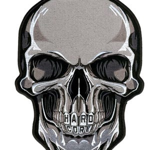 May include: A gray embroidered skull patch with the word "HARDCORE" written in black letters across the teeth.