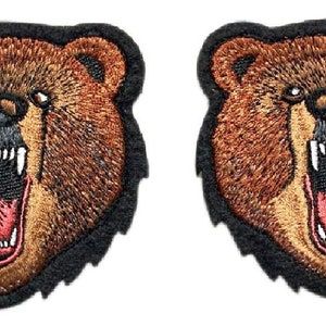 May include: Two embroidered patches depicting a brown bear with a black nose and open mouth showing teeth. The bear's fur is brown with a black outline. The patches are on a black background.