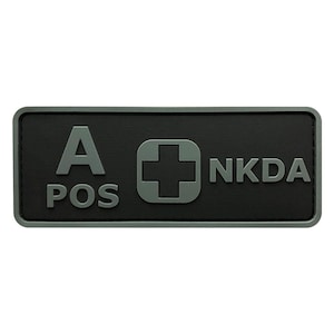 May include: A black rectangular patch with white text that reads "A POS" and "NKDA". A white plus sign is in the center of the patch.