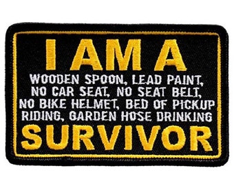 May include: Black embroidered patch with yellow text that reads "I AM A WOODEN SPOON, LEAD PAINT, NO CAR SEAT, NO SEAT BELT, NO BIKE HELMET, BED OF PICKUP RIDING, GARDEN HOSE DRINKING SURVIVOR"