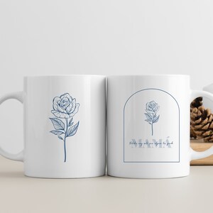 Pode incluir: Duas canecas de cer&acirc;mica branca com desenhos florais azuis. Uma caneca apresenta uma &uacute;nica rosa com caule e folhas. A outra caneca apresenta uma rosa em um arco com o texto "MAM&Aacute;" e "Pido muy alto para alguien tan grande".
