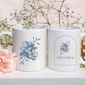 Pode incluir: Duas canecas de cer&acirc;mica branca com desenhos florais azuis. Uma caneca tem o texto "MAM&Aacute;" com a frase "Palabras muy  ante por alguien tan  grande" abaixo.