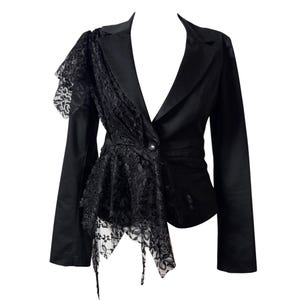 Könnte beinhalten: Ein schwarzer Blazer mit einem Knopfverschluss und steigendem Revers. Die rechte Seite des Kleidungsstücks ist mit einem asymmetrischen Überwurf aus schwarzer Blumenspitze verziert, der von der Schulter bis zu einem spitz zulaufenden Saum reicht.