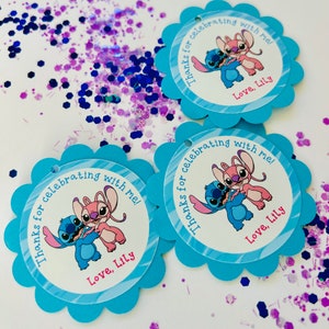 K&ouml;nnte beinhalten: Drei blaue und wei&szlig;e Geschenkanh&auml;nger mit gewelltem Rand. Jeder Anh&auml;nger zeigt ein Cartoon-Bild von Stitch und Angel aus dem Disney-Film Lilo & Stitch. Der Text auf den Anh&auml;ngern lautet "Danke, dass du mit mir gefeiert hast! Liebe, Lily."