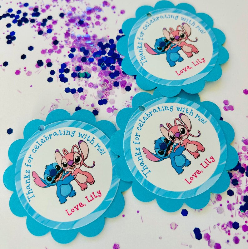 K&ouml;nnte beinhalten: Drei blaue und wei&szlig;e Geschenkanh&auml;nger mit gewelltem Rand. Jeder Anh&auml;nger zeigt ein Cartoon-Bild von Stitch und Angel aus dem Disney-Film Lilo & Stitch. Der Text auf den Anh&auml;ngern lautet "Danke, dass du mit mir gefeiert hast! Liebe, Lily."