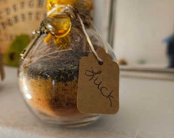 May include: A glass jar with a yellow lid and a brown tag that says "Luck". The jar is filled with herbs and spices.