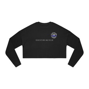 Peut inclure: Sweat-shirt noir à manches longues et coupe courte avec un motif de tournesol avec un ruban bleu. Le texte "Because he's mine I walk this line" est imprimé sous le motif.