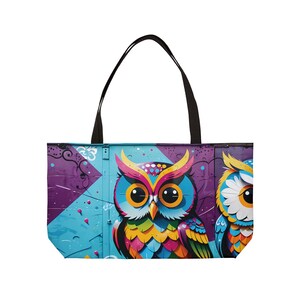 Puede incluir: Una bolsa de tela colorida con un gráfico de dos búhos. Los búhos están pintados en colores brillantes, incluyendo azul, amarillo, rosa y verde. La bolsa tiene asas negras y un fondo morado y azul.