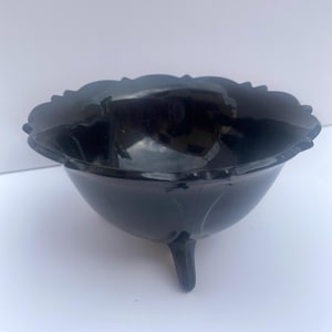 May include: A black glass bowl with a scalloped rim and three small feet. The bowl has a glossy finish and a rounded shape, suitable for serving or display.