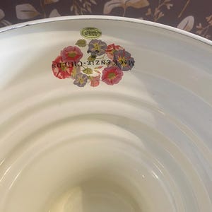 May include: Cream-colored enamelware basin with a floral decal featuring red, pink, and purple flowers. The words "MACKENZIE-CHILDS" are printed on the side. A small sticker reads "MADE IN CHINA".
