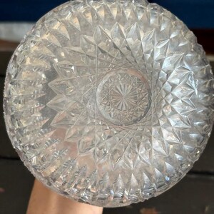 May include: Clear glass bowl with a detailed geometric pattern. The bowl's base features a starburst design, and the sides are covered in diamond-shaped facets. The bowl is held by a person.