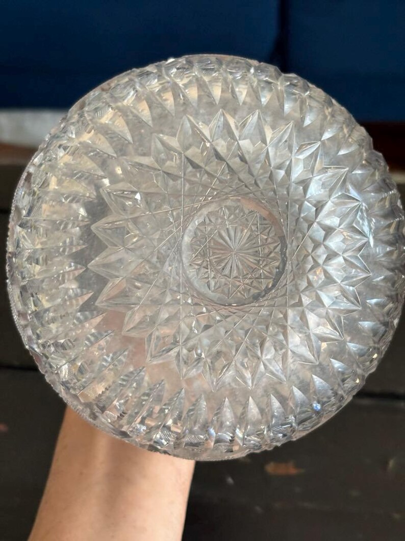 May include: Clear glass bowl with a detailed geometric pattern. The bowl's base features a starburst design, and the sides are covered in diamond-shaped facets. The bowl is held by a person.