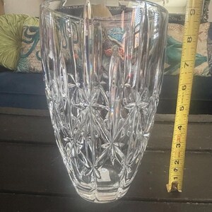 May include: A clear, cut-glass vase with a starburst pattern and vertical lines. The vase is approximately 20 cm tall. A yellow measuring tape is next to the vase.
