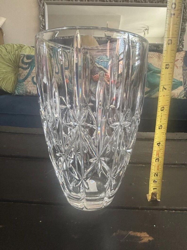 May include: A clear, cut-glass vase with a starburst pattern and vertical lines. The vase is approximately 20 cm tall. A yellow measuring tape is next to the vase.