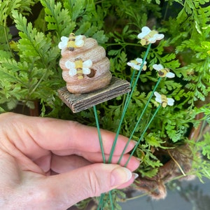 Puede incluir: Un conjunto de cinco estacas metálicas verdes con figuritas de abejas adheridas. Las abejas son amarillas y negras con alas blancas. Una estaca presenta una pequeña colmena marrón y amarilla con abejas en el lateral.
