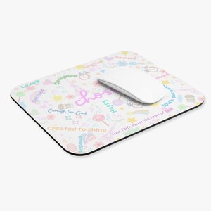 May include: White rectangular mousepad with a black border, covered in colorful doodles and inspirational words like "Loved" and "Happy." A white computer mouse rests on the pad. The word "Chosen" is in the center.