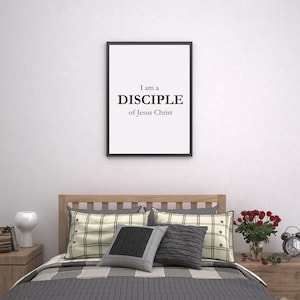 May include: A black framed print with the text "I am a DISCIPLE of Jesus Christ" hanging on a white wall above a bed with a wooden headboard and gray and white checkered bedding.