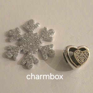 May include: A silver and gold charm in the shape of two interlocking hearts. The smaller heart is set with clear cubic zirconia stones.